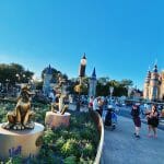 Foto do castelo da Cinderela no Magic Kingdom. Há estátuas do Pluto no jardim, e pessoas andando em volta.