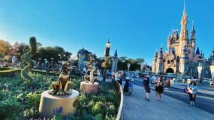 Foto do castelo da Cinderela no Magic Kingdom. Há estátuas do Pluto no jardim, e pessoas andando em volta.