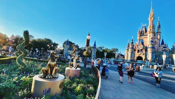 Foto do castelo da Cinderela no Magic Kingdom. Há estátuas do Pluto no jardim, e pessoas andando em volta.