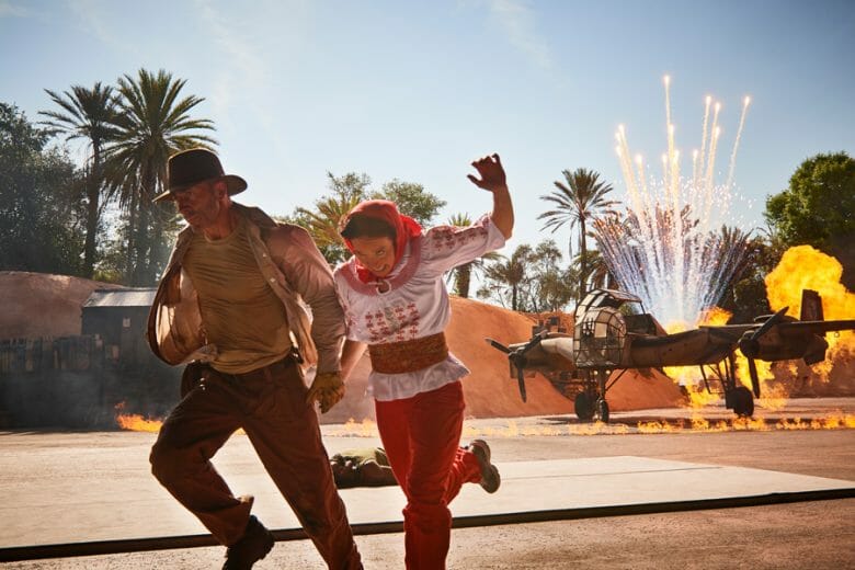 Imagem de dois atores durante o show do Indiana Jones, com um avião soltando fagulhas atrás 