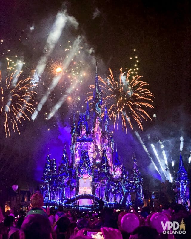 Foto vertical do show de fogos Disney Enchantment. O castelo está iluminado em tons de roxo e dá pra ver a silhueta do Peter Pan em projeção.