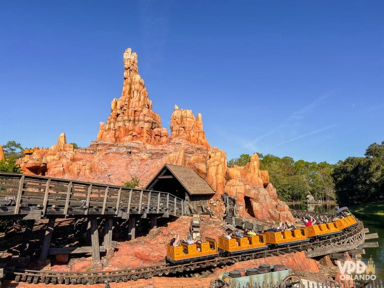 Foto do carrinho andando na Big Thunder Mountain. Há árvores ao redor e o céu está azul. Essa atração também faz parte do pacote do Genie+ no Magic Kingdom.