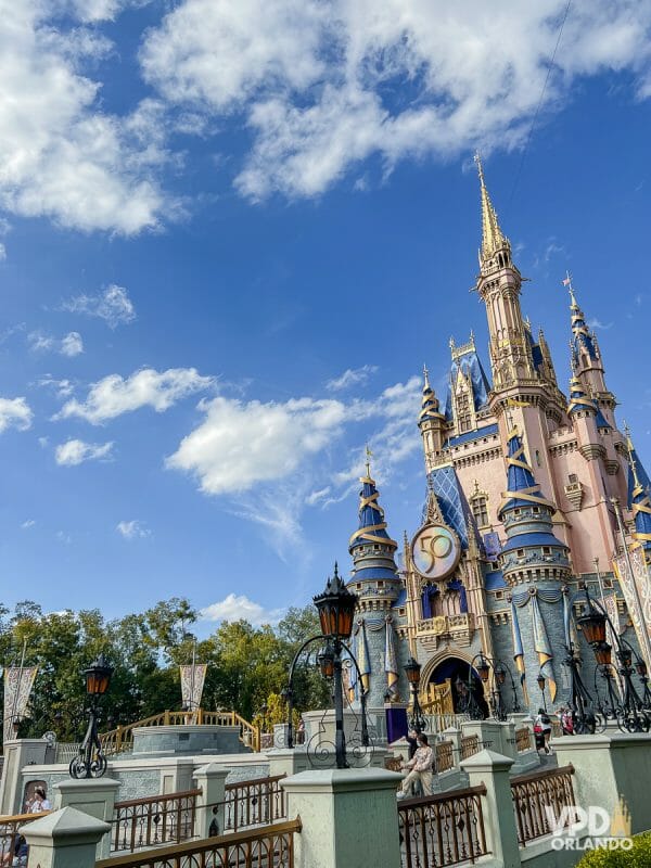 Foto do castelo da Cinderella no Magic Kingdom durante o dia, com visitantes passando ao redor. 