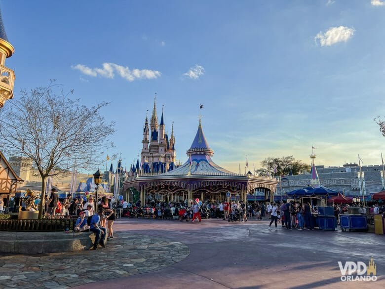 Foto da Fantasyland no Magic Kingdom no entardecer, com o castelo ao fundo e o carrossel em primeiro plano, e várias pessoas caminhando ao redor dele.