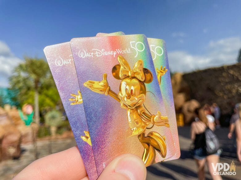 Foto de 3 ingressos da Disney sendo segurados. Eles são holográficos, e o primeiro deles traz a Minnie em dourado.