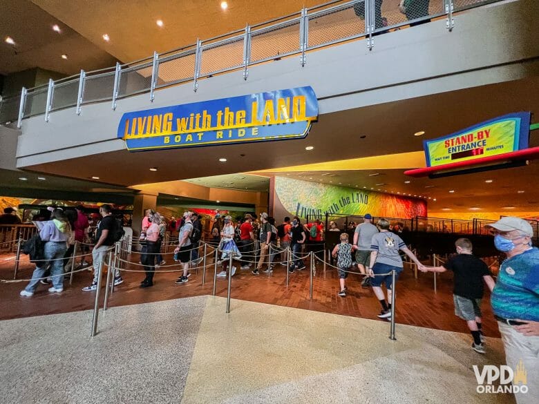 Foto da fachada do Living With The Land, uma das atrações disponíveis no Genie+ do Epcot. A placa é azul com letras amarelas, e há pessoas na fila.