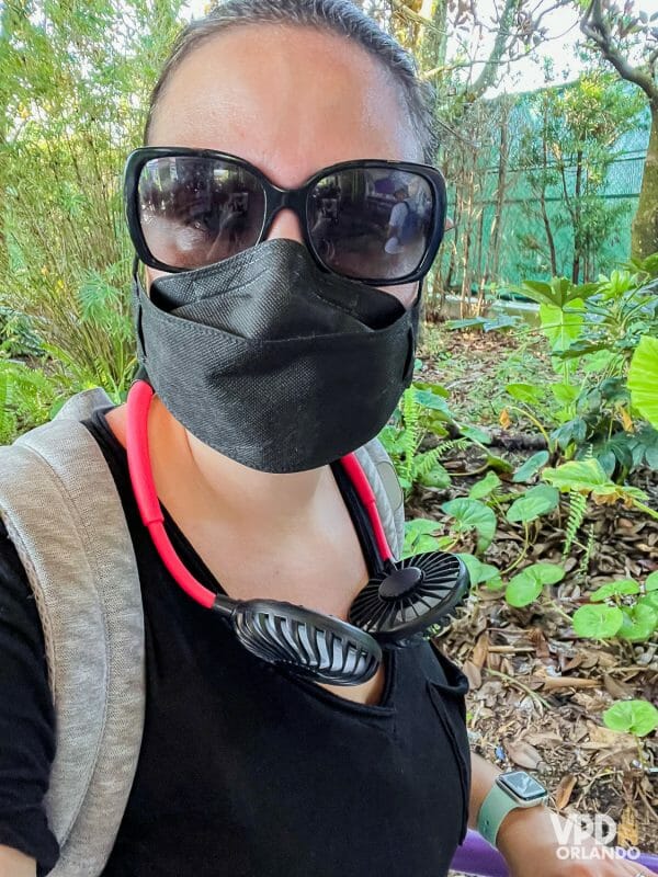 Foto da Re usando óculos de sol e ventilador de pescoço vermelho e preto em um dia de calor nos parques.