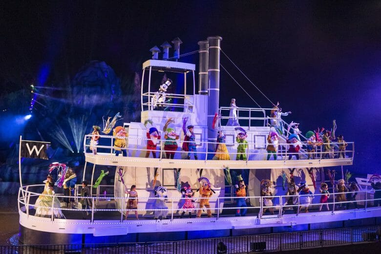 foto do barco do fantasmic com vários personagens, incluindo mickey, minnie, pateta, os sete anões, princesas e mais. eles seguram bandeiras coloridas.
