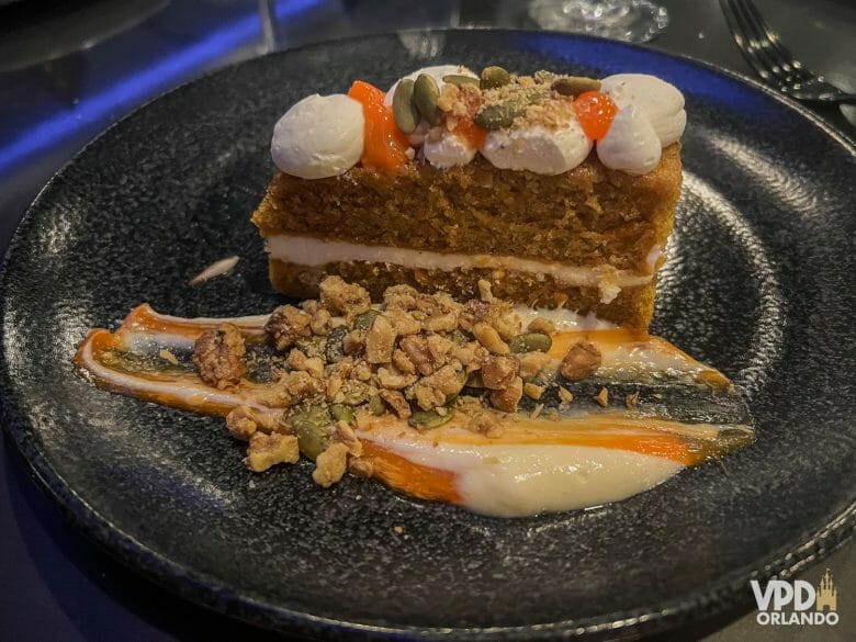 Foto de uma sobremesa, um bolo de cenoura americano com várias sementes e nozes ao redor.