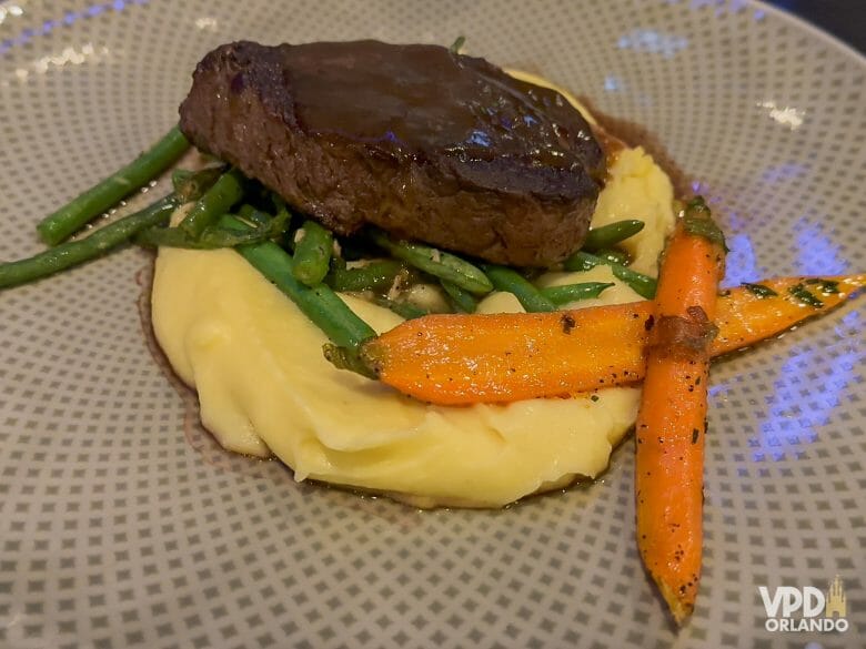 Foto de uma carne vermelha junto com um purê e cenouras.