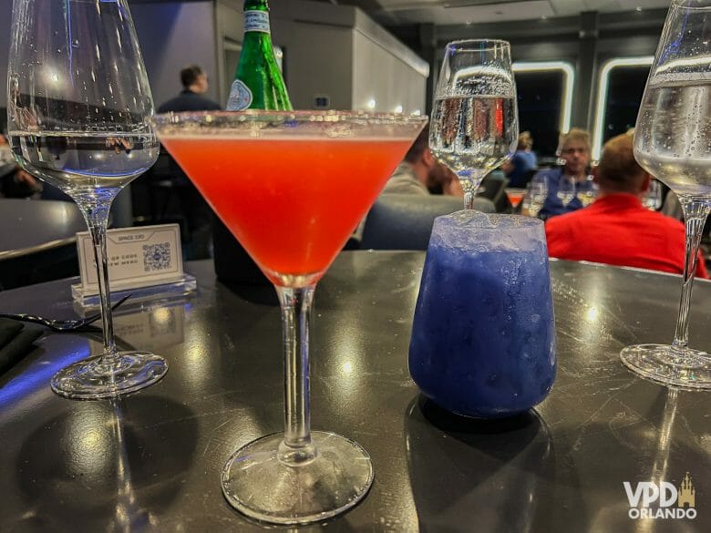 Dois copos de drink do Space 220. Um está em um copo de martini e é vermelho, outro é azul e está em um copo menor.