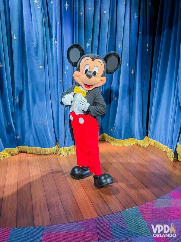 Foto do Mickey Mouse em frente a uma cortina azul. Os encontros com personagens tem filas longas no fim de ano.