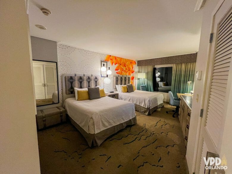 Foto do quarto do Royal Pacific, com duas camas queens com roupa de cama branca. A parede ao fundo tem um papel de parede com flores laranjas.
