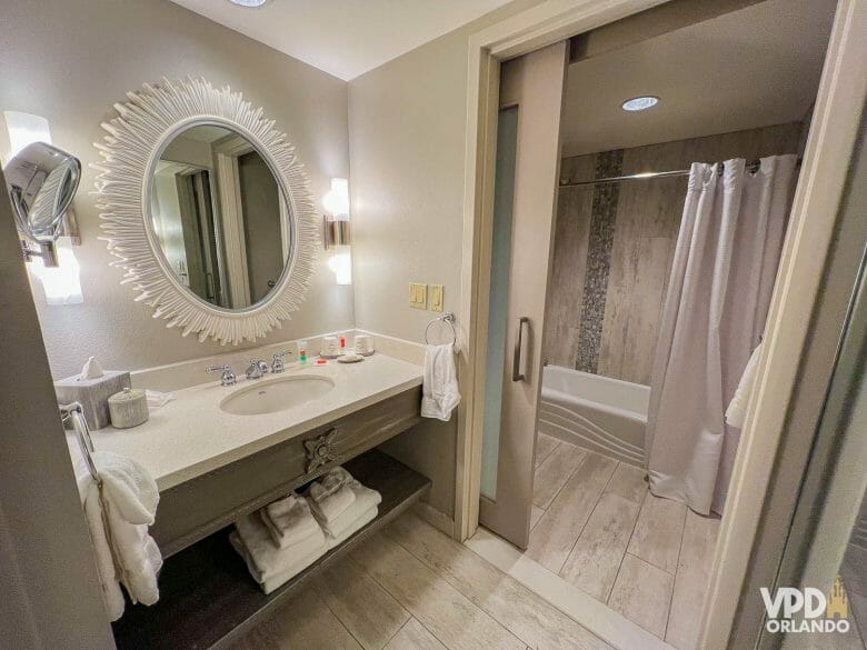 Foto do banheiro do Royal Pacific, com uma pia branca, espelho e várias toalhas, e do lado direito um chuveiro com banheira.