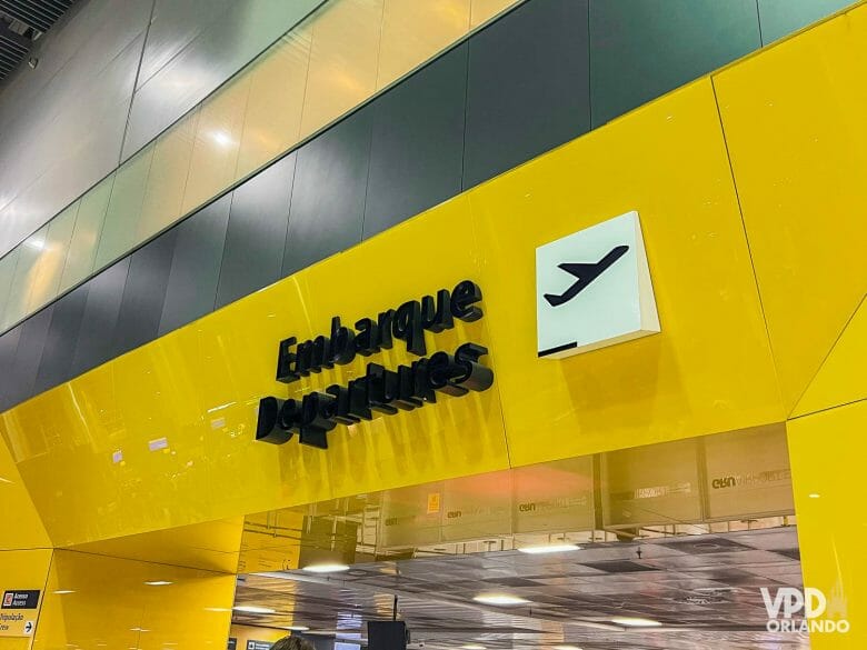 Foto da área de embarque do aeroporto de Guarulhos, com o fundo amarelo e texto em preto. Os requisitos para voltar ao Brasil atualmente mudaram!