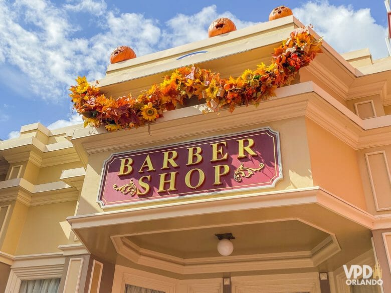 Placa do Harmony Barber Shop, com o nome escrito em uma placa vermelha. Há decorações de Halloween e outono em cima.