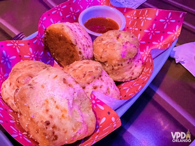 Foto dos biscuits do roundup rodeo bbq, servidos em uma travessa com um papel vermelho e um potinho de molho.