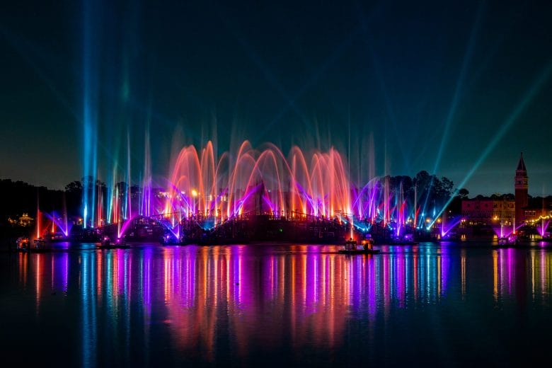 Foto oficial do Luminous, com raios coloridos saindo de uma estrutura no meio do lago do Epcot.