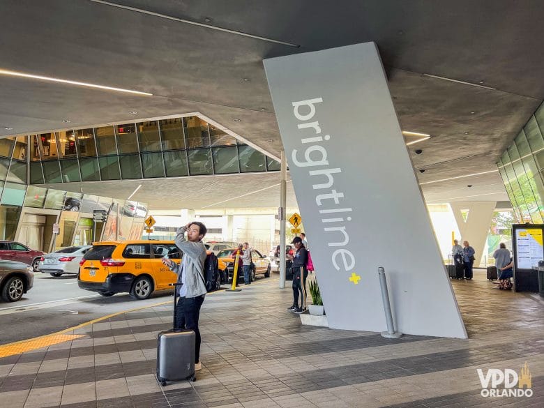 parte externa da estação de trem, com um letreiro de brightline escrito em branco e carros no embarque e desembarque.