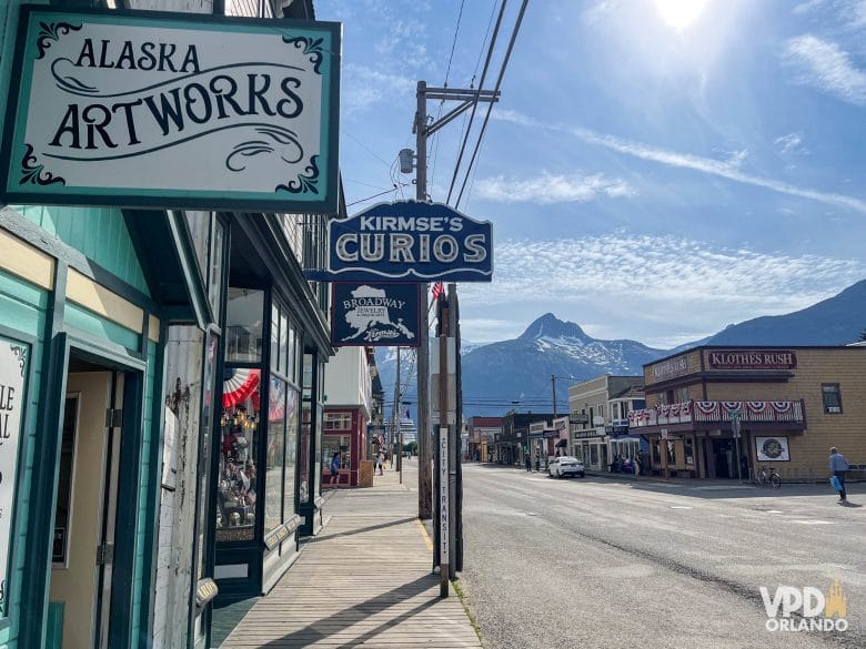 rua com diversas placas e montanhas ao fundo, na cidade de Skagway