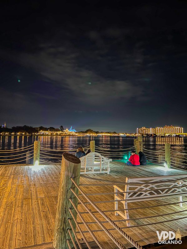 vista do pier do grand floridian à noite, com bancos espalhados. ao fundo é possível ver o parque.