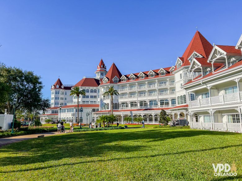 Prédio do grand floridian. Ele é branco e tem cerca de 3 andares, várias varandas e um telhado vermelho, e é rodeado por um gramado verde.